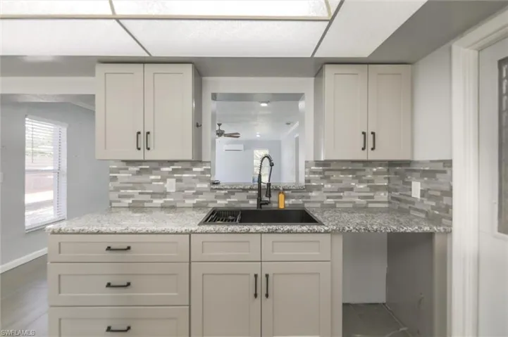 Kitchen with decorative backsplash, sink, white cabinets, and light stone countertops