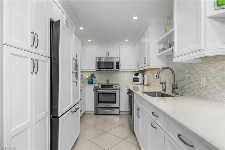 Kitchen with sink, white cabinets, light tile patterned floors, light stone counters, and stainless steel appliances