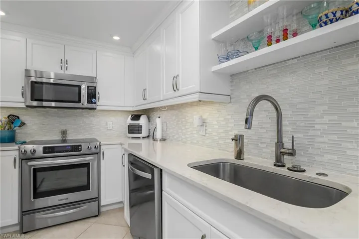 Kitchen featuring sink, appliances with stainless steel finishes, light stone countertops, white cabinets, and light tile patterned flooring