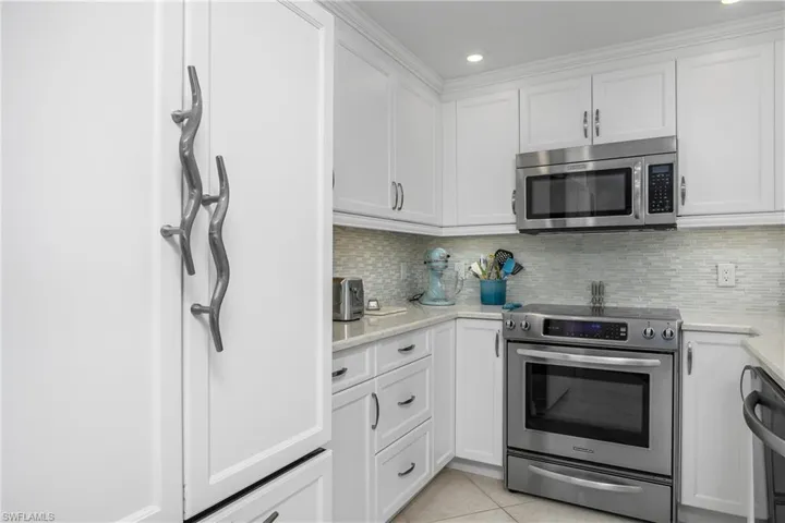Kitchen featuring white cabinetry, stainless steel appliances, light tile patterned flooring, and decorative backsplash