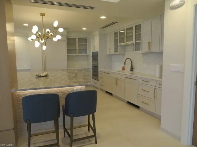 Social room kitchen with decorative backsplash, glass insert cabinets, recessed lighting, hanging light fixtures, and a kitchen bar