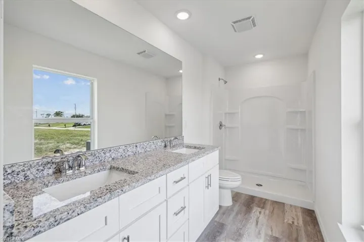 Bathroom with dual bowl vanity, hardwood / wood-style floors, walk in shower, and toilet