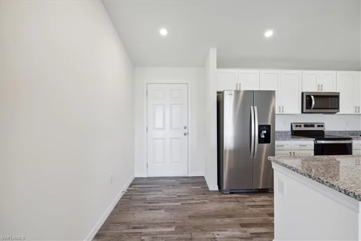 Kitchen featuring stainless steel appliances, wood-type flooring, white cabinetry, and light stone countertops