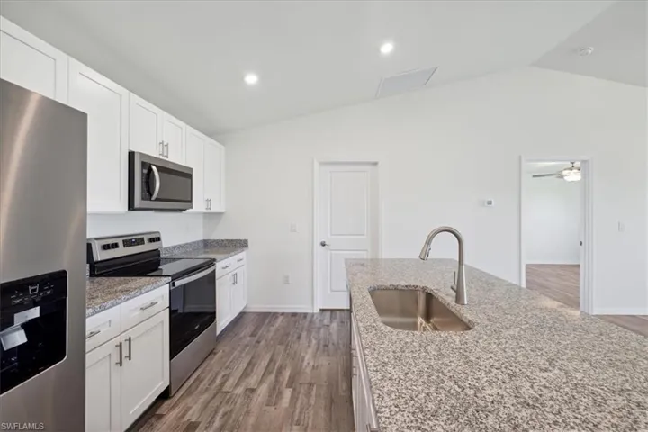Kitchen with ceiling fan, hardwood / wood-style floors, appliances with stainless steel finishes, sink, and lofted ceiling