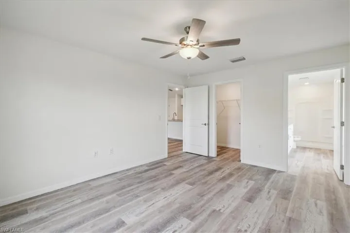 Unfurnished bedroom featuring light hardwood / wood-style floors, a walk in closet, ensuite bathroom, and ceiling fan