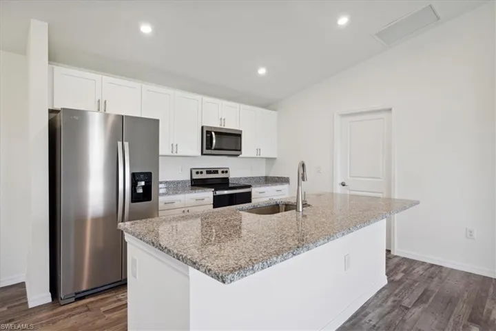 Kitchen featuring appliances with stainless steel finishes, white cabinetry, an island with sink, and dark hardwood / wood-style flooring