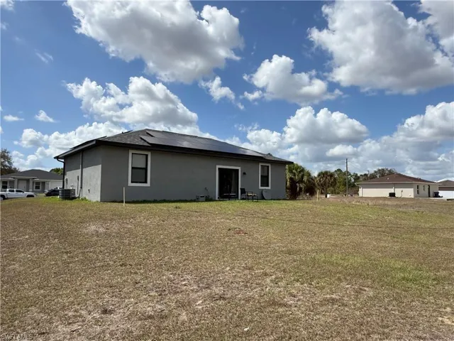 Back of house with roof mounted solar panels, stucco siding, and a lawn