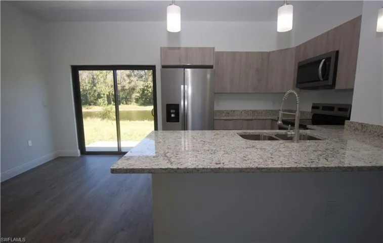Kitchen featuring light stone countertops, a peninsula, stainless steel appliances, and decorative light fixtures