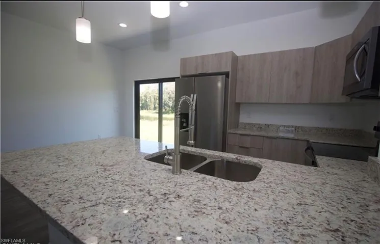 Kitchen with light stone counters, range with electric stovetop, stainless steel refrigerator with ice dispenser, a peninsula, and modern cabinets