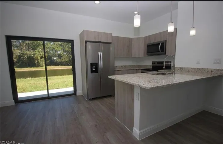 Kitchen featuring hanging light fixtures, light stone countertops, stainless steel appliances, dark wood-style floors, and a peninsula