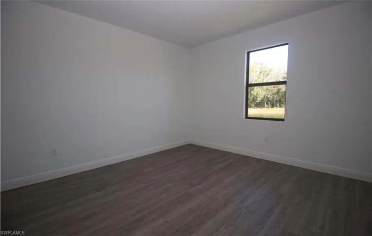 Empty room with dark wood-type flooring and baseboards