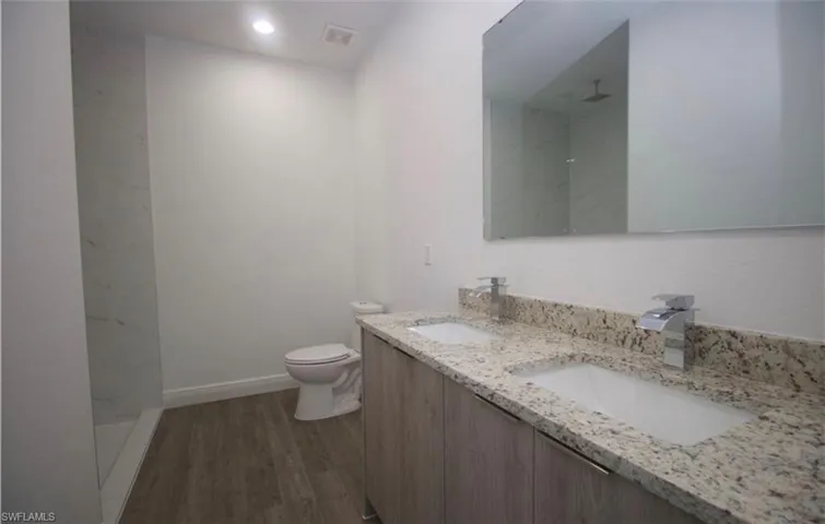Full bathroom featuring double vanity, dark wood-style floors, a marble finish shower, and recessed lighting