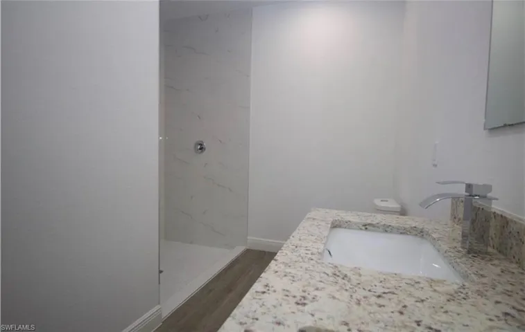Bathroom featuring vanity, a marble finish shower, and dark wood-style floors