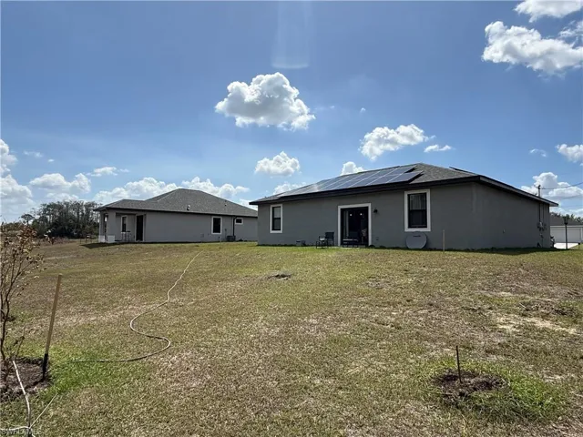 Rear view of house featuring solar panels, stucco siding, and a lawn