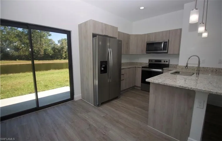 Kitchen featuring light stone counters, stainless steel appliances, decorative light fixtures, a peninsula, and modern cabinets