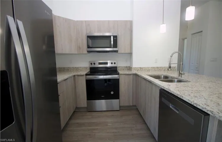 Kitchen with light stone countertops, stainless steel appliances, light wood finish cabinets, a peninsula, and hanging light fixtures