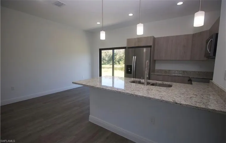 Kitchen with light stone counters, stainless steel appliances, a peninsula, and hanging light fixtures