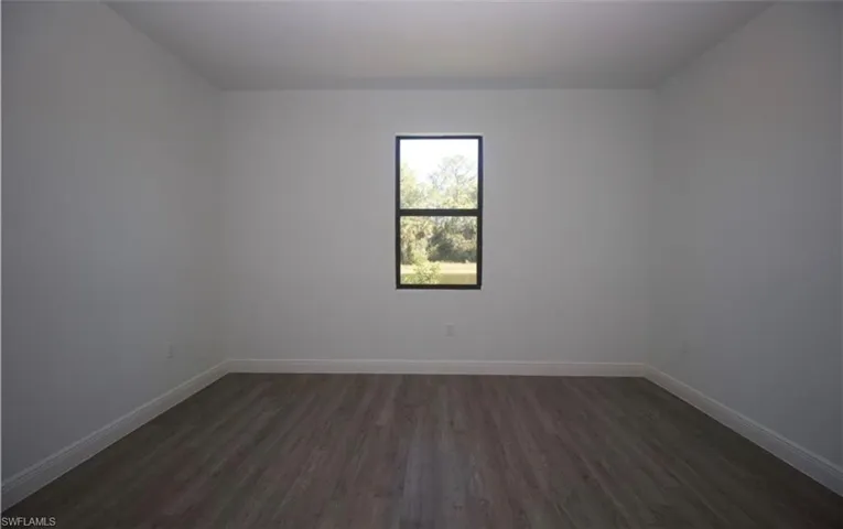 Empty room featuring dark wood finished floors and baseboards