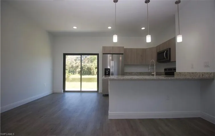 Kitchen with light stone countertops, a peninsula, stainless steel appliances, pendant lighting, and dark wood finished floors