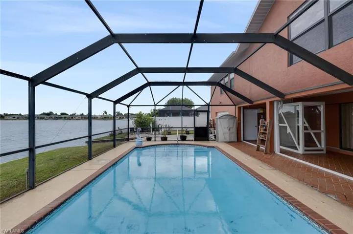 Outdoor pool featuring a sunroom, glass enclosure, a water view, and a patio