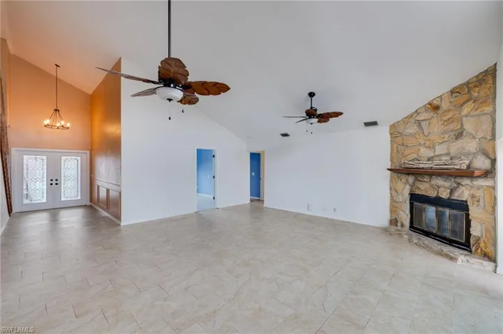 Unfurnished living room featuring high vaulted ceiling, a chandelier, a fireplace, and french doors
