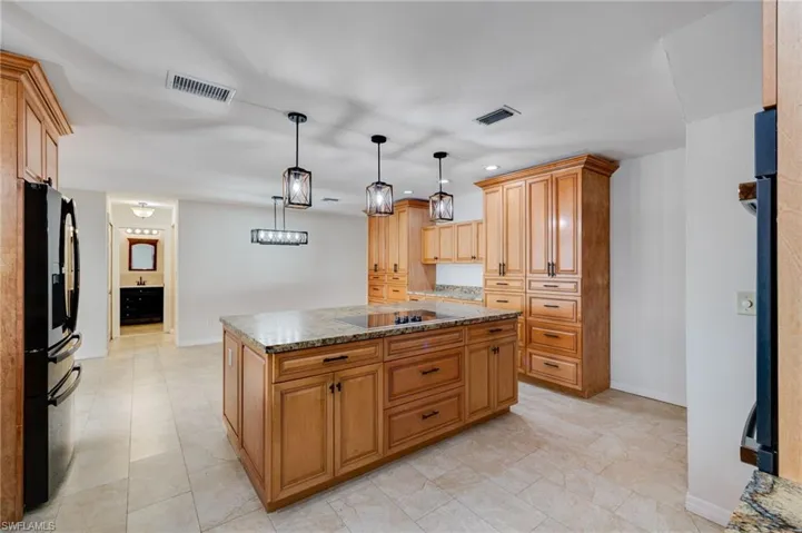 Kitchen with decorative light fixtures, black appliances, a kitchen island, recessed lighting, and light stone countertops