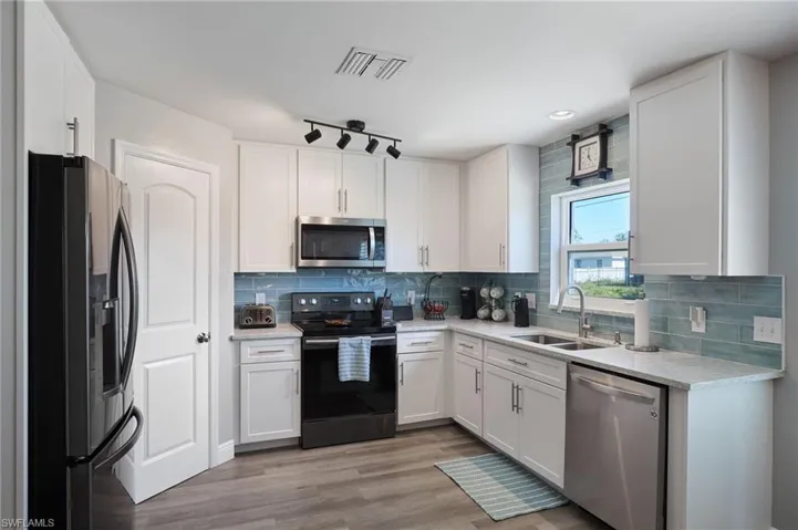 Kitchen with white cabinets, sink, stainless steel appliances, and light hardwood / wood-style flooring