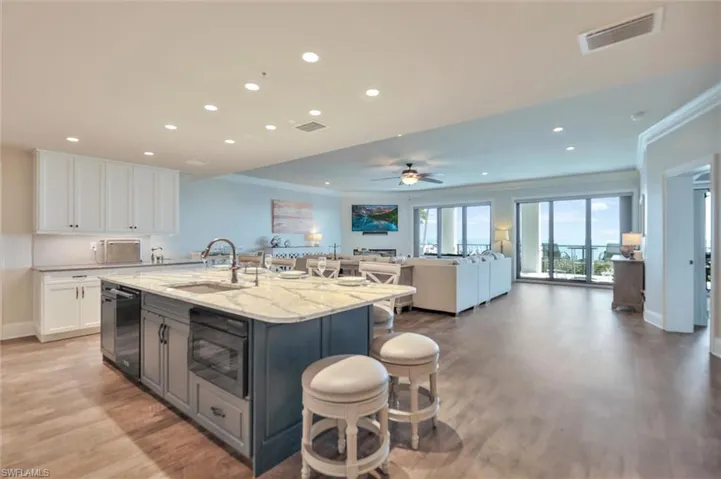 Dual tone kitchen featuring crown molding, light stone countertops, two tone cabinetry, a kitchen bar, and recessed lighting