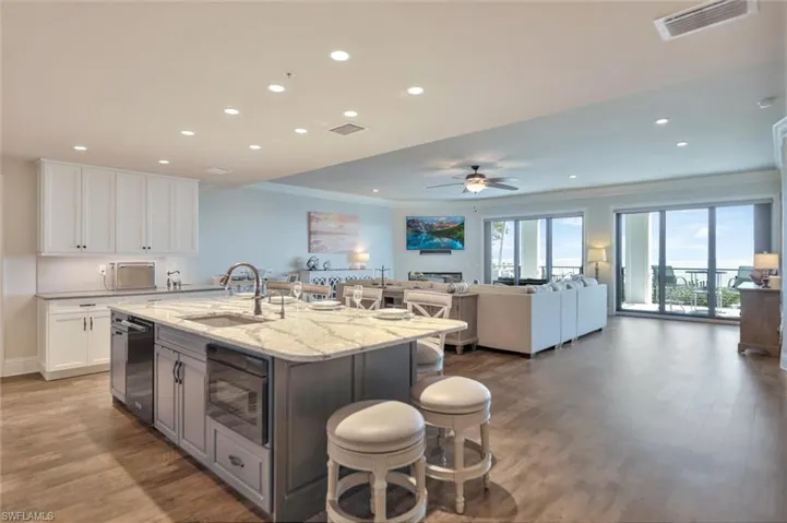 Two tone kitchen with crown molding, a breakfast bar area, light stone counters, dual tone cabinetry, and light wood-type flooring