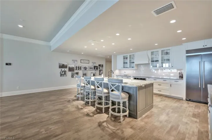 Two tone kitchen with stainless steel appliances, a breakfast bar, a center island with sink, glass insert cabinets, and recessed lighting