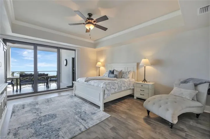 Bedroom featuring a raised ceiling, access to outside, ceiling fan, wood finished floors, and crown molding