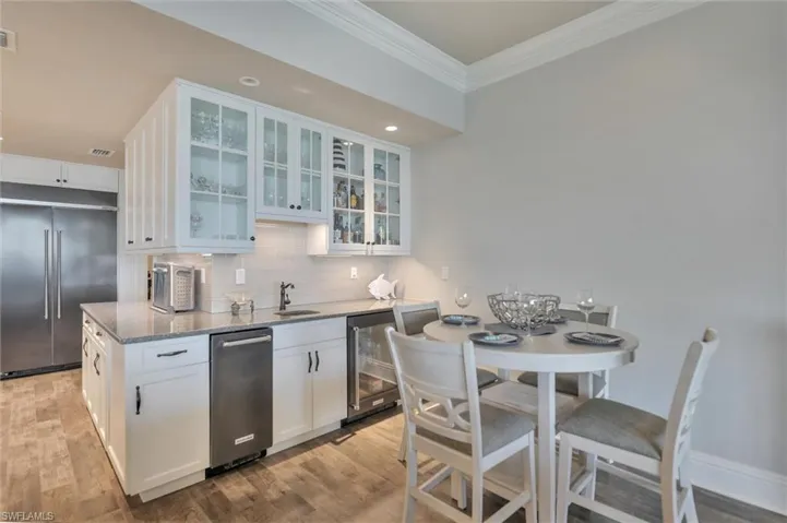 Kitchen featuring stainless steel appliances, white cabinets, light stone countertops, light wood-type flooring, and crown molding