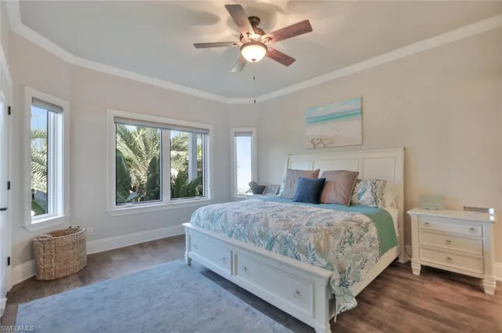 Bedroom with ornamental molding, dark wood-type flooring, and ceiling fan