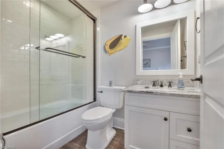 Full bathroom featuring vanity, dark wood-style floors, and combined bath / shower with glass door