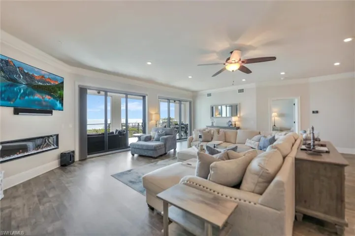 Living room with wood finished floors, ornamental molding, a ceiling fan, a glass covered fireplace, and recessed lighting