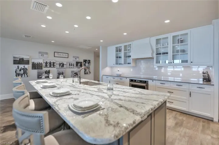 Kitchen featuring light wood-style floors, light stone counters, a kitchen bar, a large island, and recessed lighting