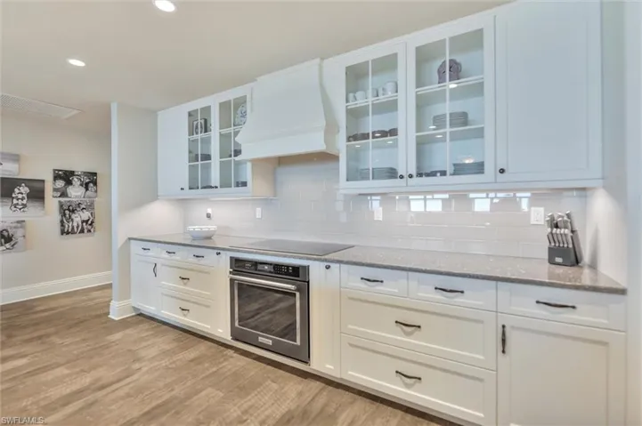 Kitchen with stainless steel oven, light stone countertops, white cabinetry, glass fronted cabinets, and recessed lighting