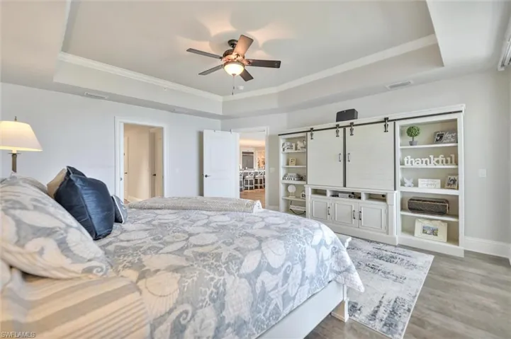 Bedroom with a raised ceiling, ornamental molding, light wood-style flooring, and a ceiling fan