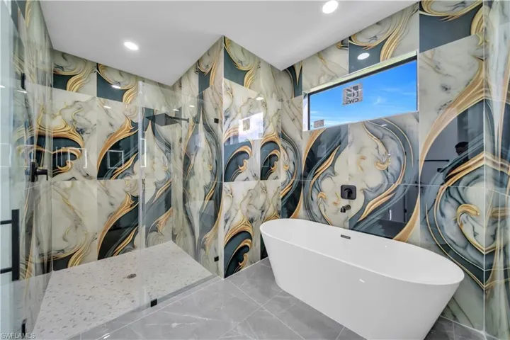 Detailed view of a marble finish shower, a freestanding bath, recessed lighting, and tile walls