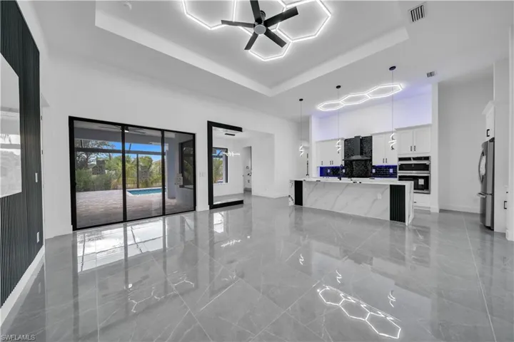 Kitchen with ceiling fan, a raised ceiling, white cabinets, wall chimney range hood, and appliances with stainless steel finishes