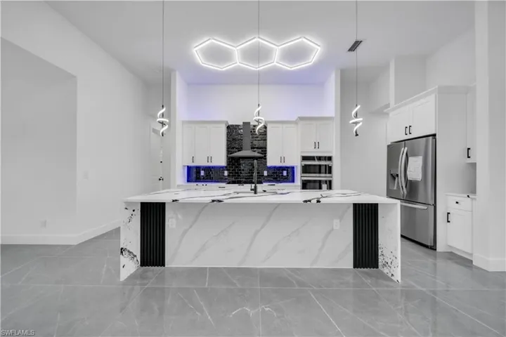 Kitchen with stainless steel appliances, white cabinetry, pendant lighting, light stone countertops, and a spacious island