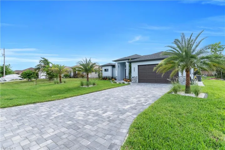 View of front of property featuring decorative driveway, stone siding, a garage, and a front lawn