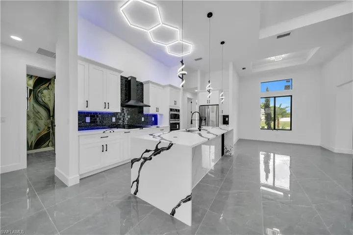Kitchen featuring wall chimney range hood, white cabinetry, stainless steel appliances, a spacious island, and a high ceiling