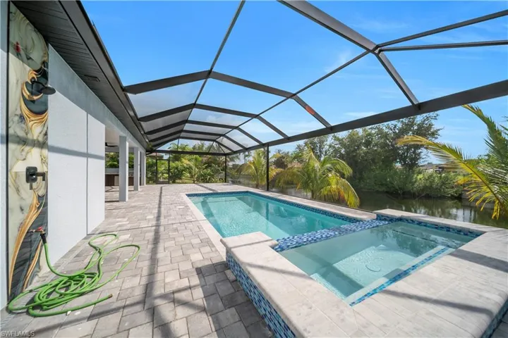View of pool featuring a patio, a pool with connected hot tub, glass enclosure, and a water view