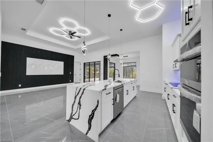 Kitchen with a raised ceiling, light marble finish flooring, appliances with stainless steel finishes, white cabinetry, and wooden walls