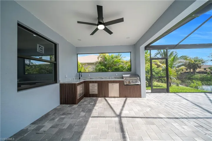 View of patio featuring exterior kitchen, a ceiling fan, and glass enclosure
