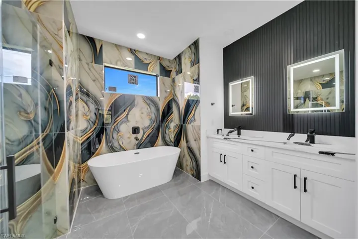 Bathroom with a soaking tub, double vanity, marble finish floors, and recessed lighting