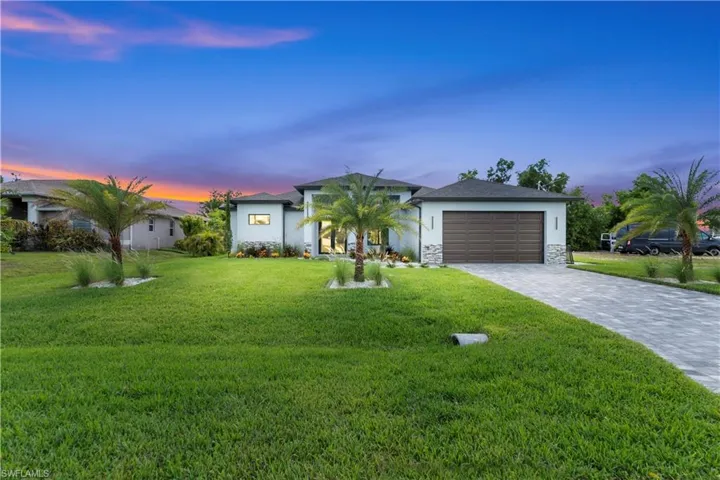 Single story home featuring an attached garage, decorative driveway, a yard, stucco siding, and stone siding