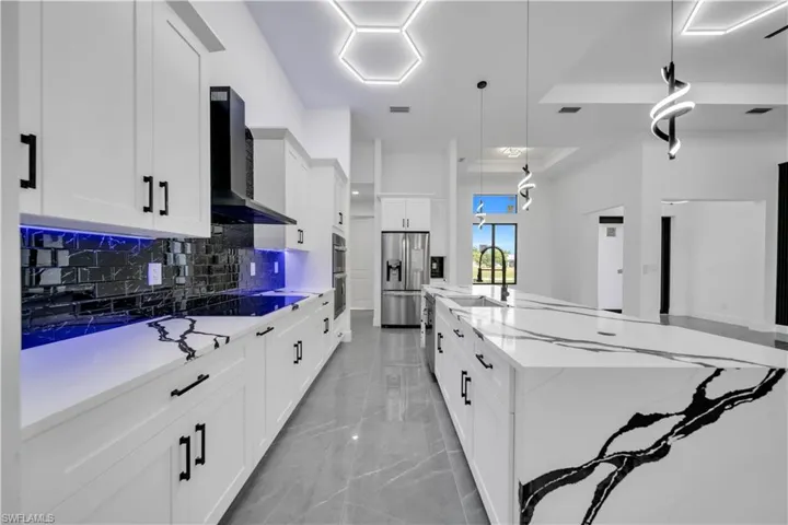 Kitchen featuring light marble finish flooring, wall chimney exhaust hood, stainless steel fridge with ice dispenser, decorative backsplash, and a spacious island