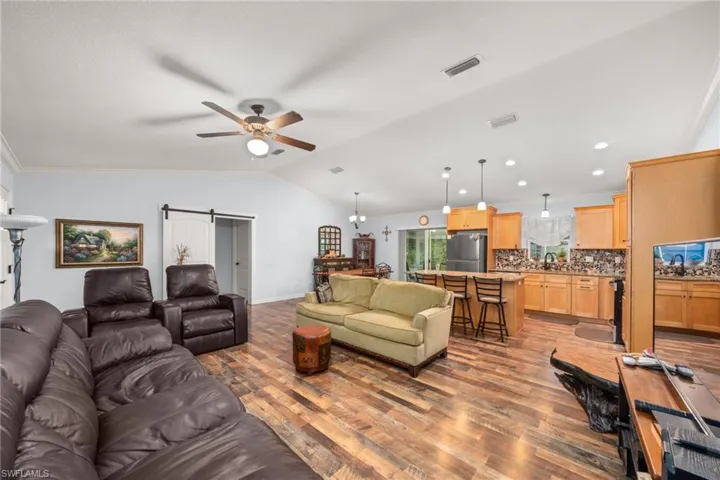 Living area with a barn door, ornamental molding, a ceiling fan, vaulted ceiling, and light wood finished floors